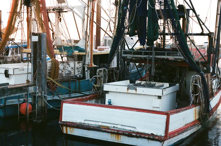 Several fishing boats with nets are docked in a harbor.