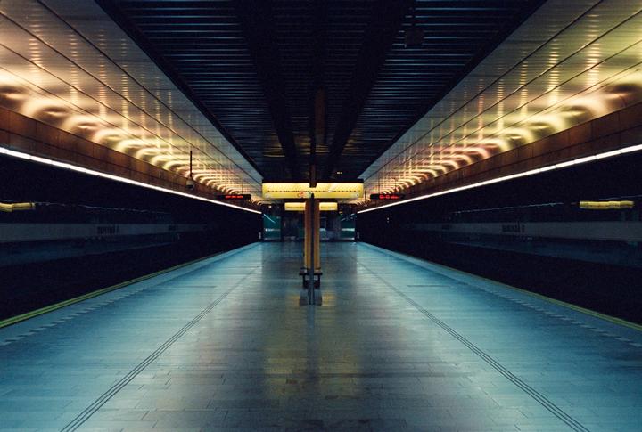 A long exposure shows an empty subway platform with illuminated ceilings and a central support column.