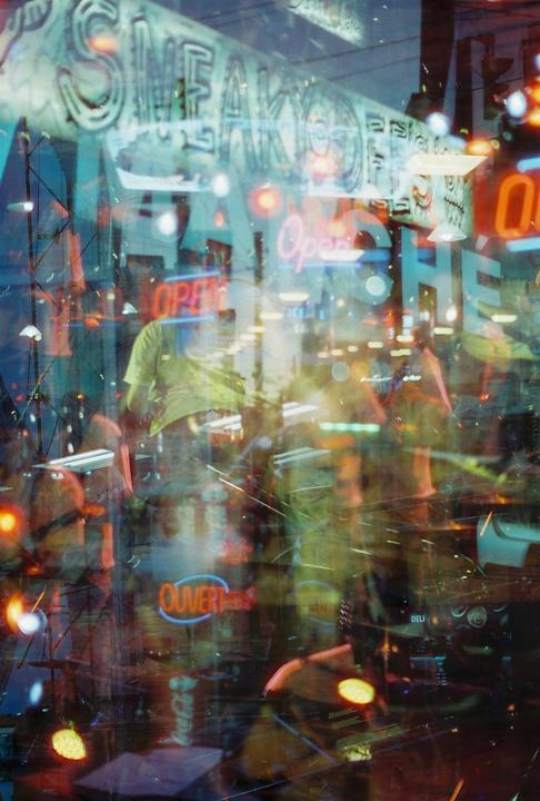 A blurry, colorful image shows multiple exposures of a street scene with neon signs and reflections.