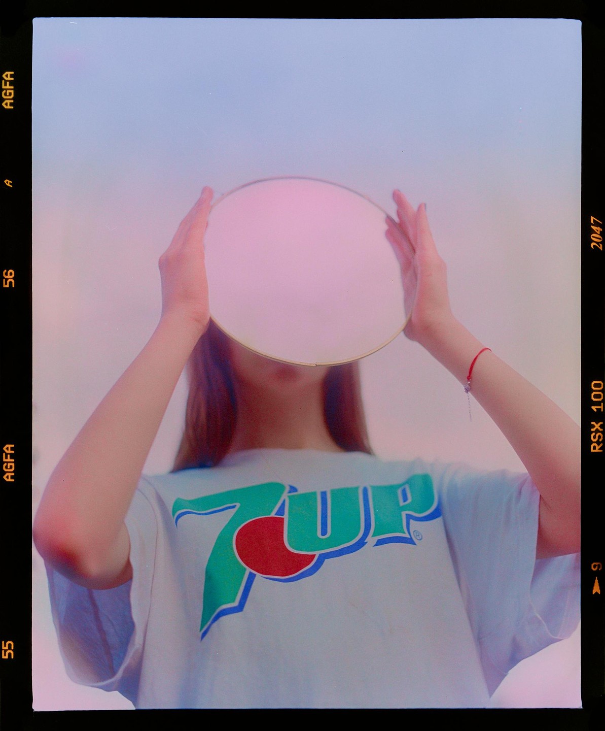 A woman holds a mirror in front of her face, obscuring it, while wearing a 7UP t-shirt.