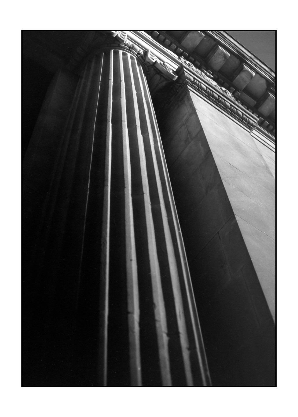 A fluted column stands next to a building with ornate architectural details.