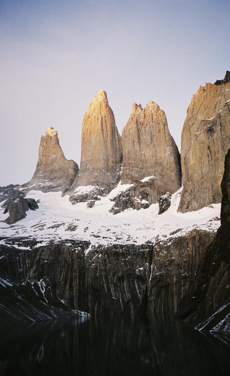 Snow-covered mountains rise above a body of water, with the peaks illuminated by golden light.
