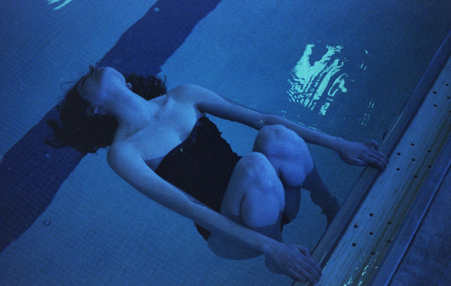A woman floats in a swimming pool, holding onto the edge.