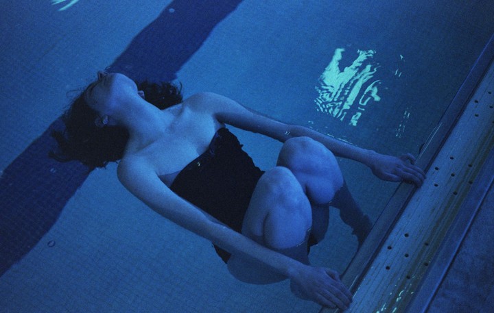 A woman floats in a swimming pool, holding onto the edge.