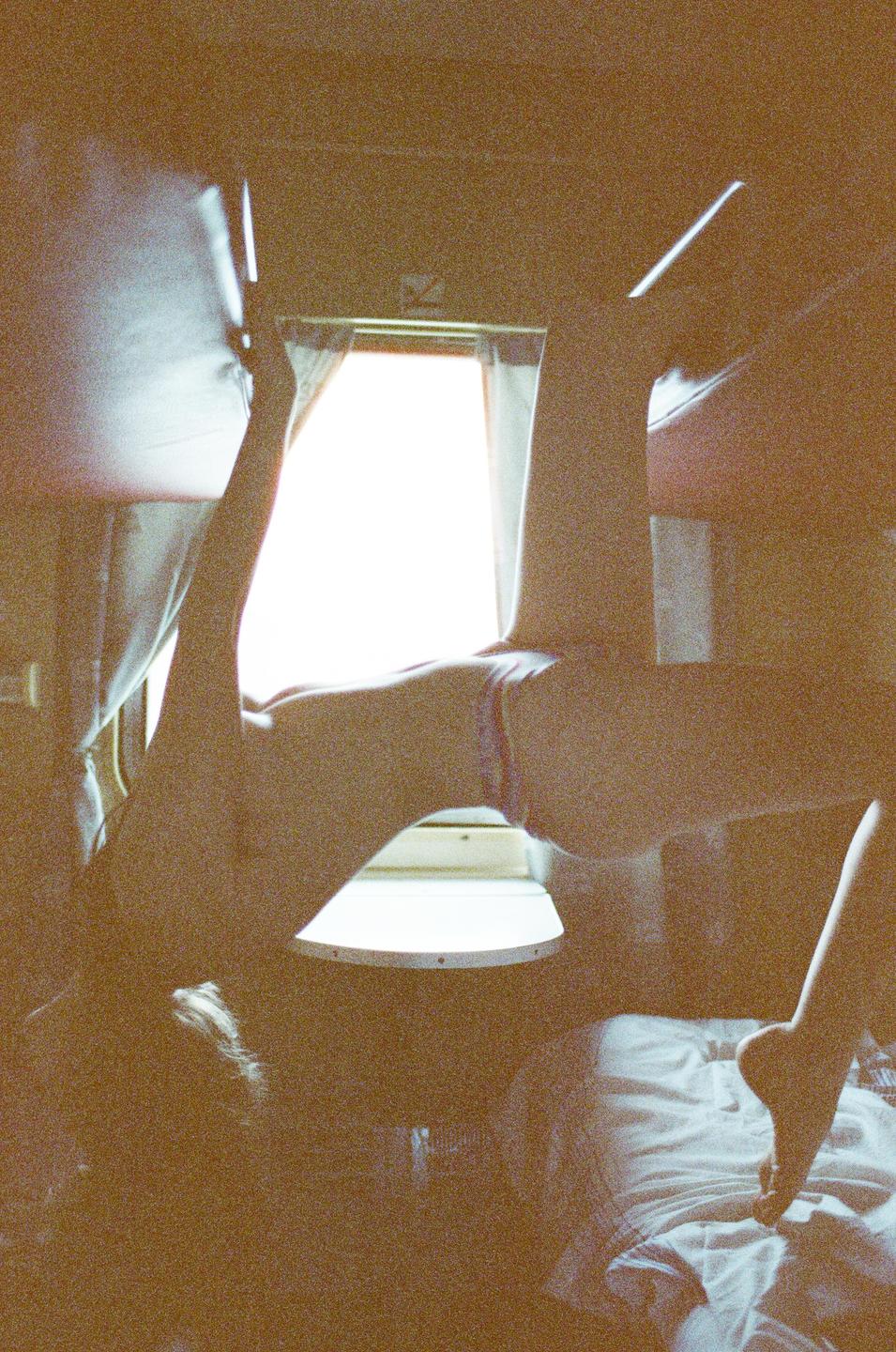 A person is upside down in a train compartment with light coming through a window.