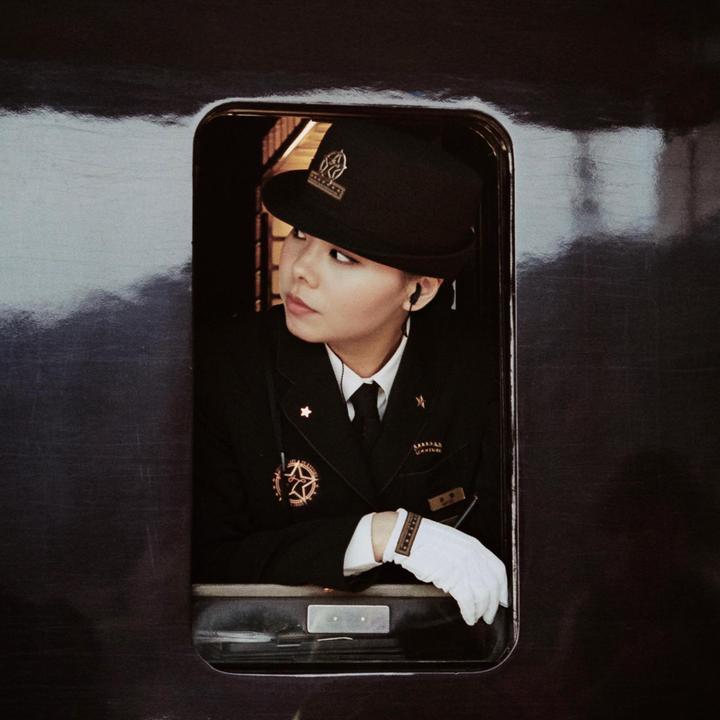 A woman in a uniform with a hat and white gloves looks out of a train window.