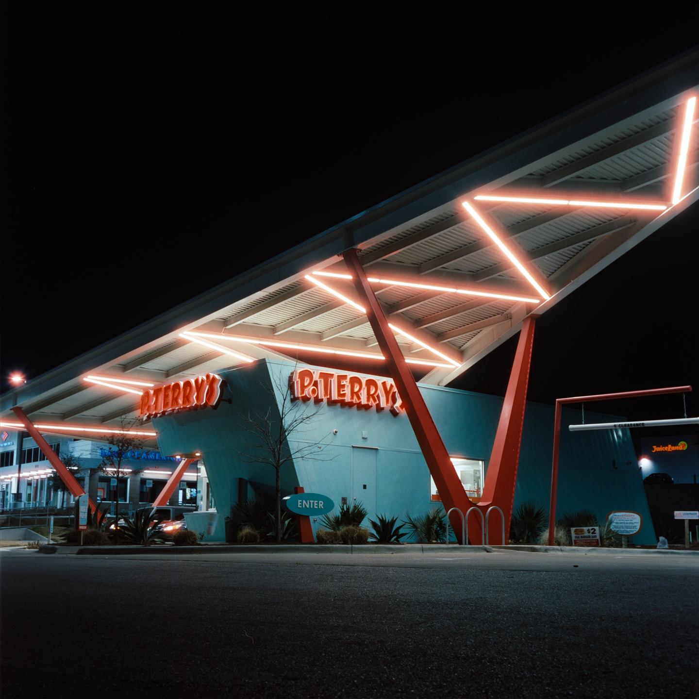 A burger restaurant with a distinctive roof structure and neon lighting is illuminated at night.