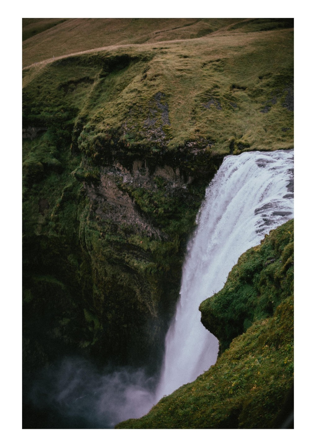A powerful waterfall cascades down a mossy cliff into a misty pool below.