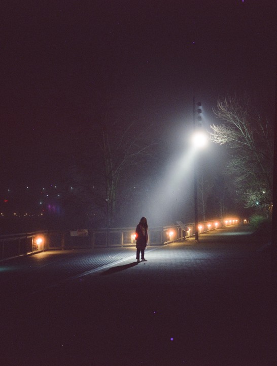 A woman stands on a path illuminated by a bright light beam at night.