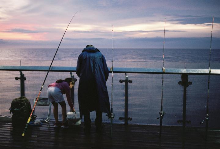 A man and a girl are fishing from a pier at dusk.