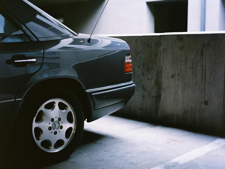 A dark sedan is parked next to a concrete wall in a parking garage.
