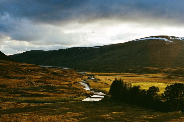 A winding river flows through a valley with mountains under a cloudy sky.