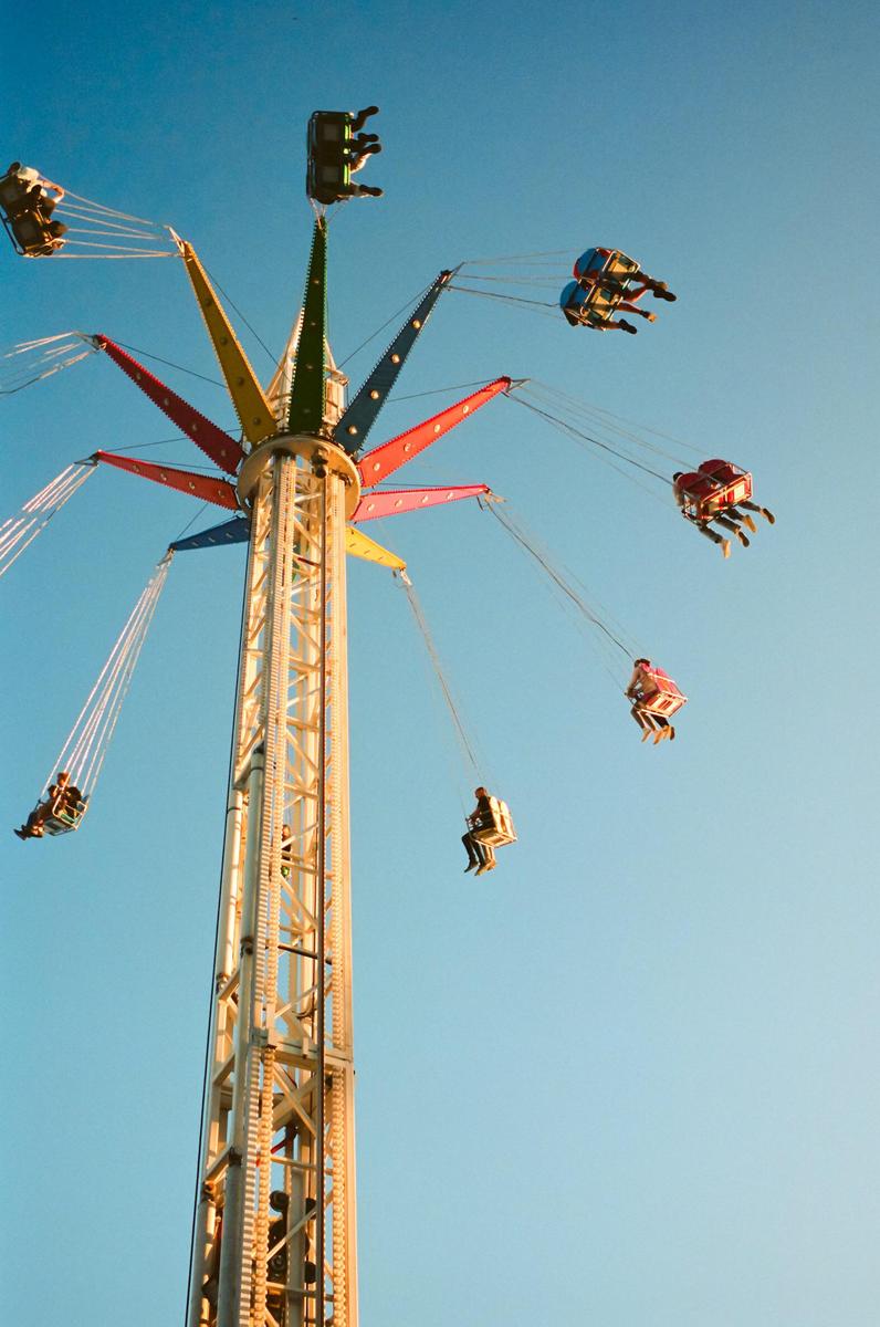 People ride a colorful swing ride against a clear blue sky.