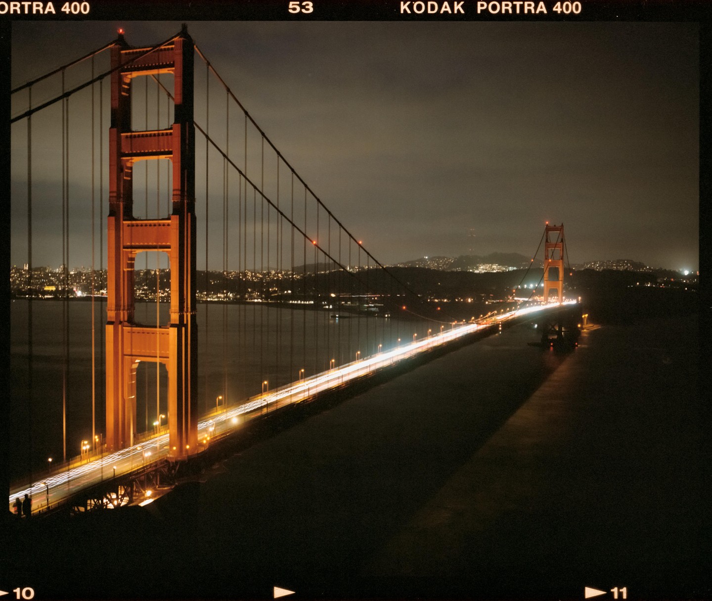 The Golden Gate Bridge is illuminated at night with car light trails on its road.