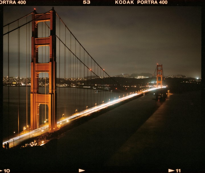 The Golden Gate Bridge is illuminated at night with car light trails on its road.