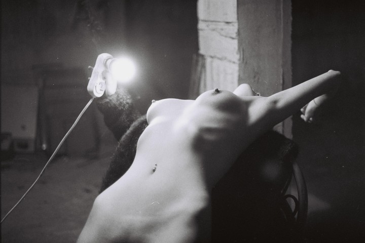A woman reclines with her torso exposed, illuminated by a bright light.
