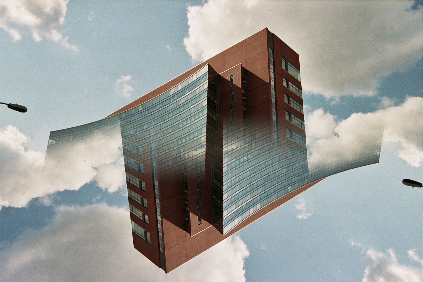 A brick building with a curved glass facade appears to float in the sky, surrounded by clouds.