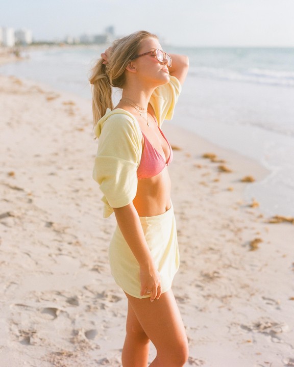 A woman stands on a sandy beach looking towards the ocean.