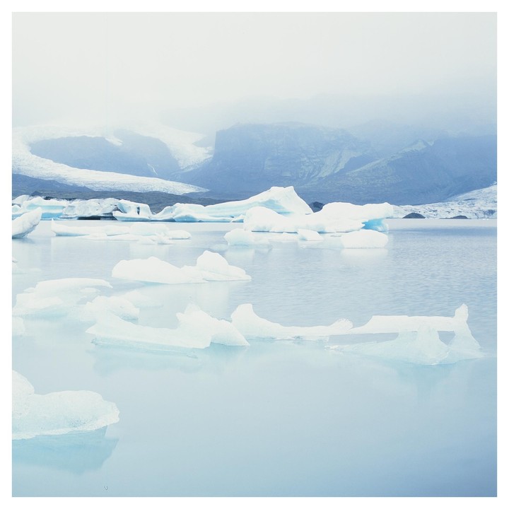Icebergs float on a glacial lagoon with mountains and a glacier in the background under a hazy sky.