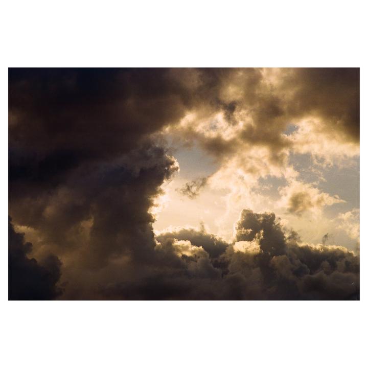 Dark storm clouds are illuminated from behind by a bright sky.