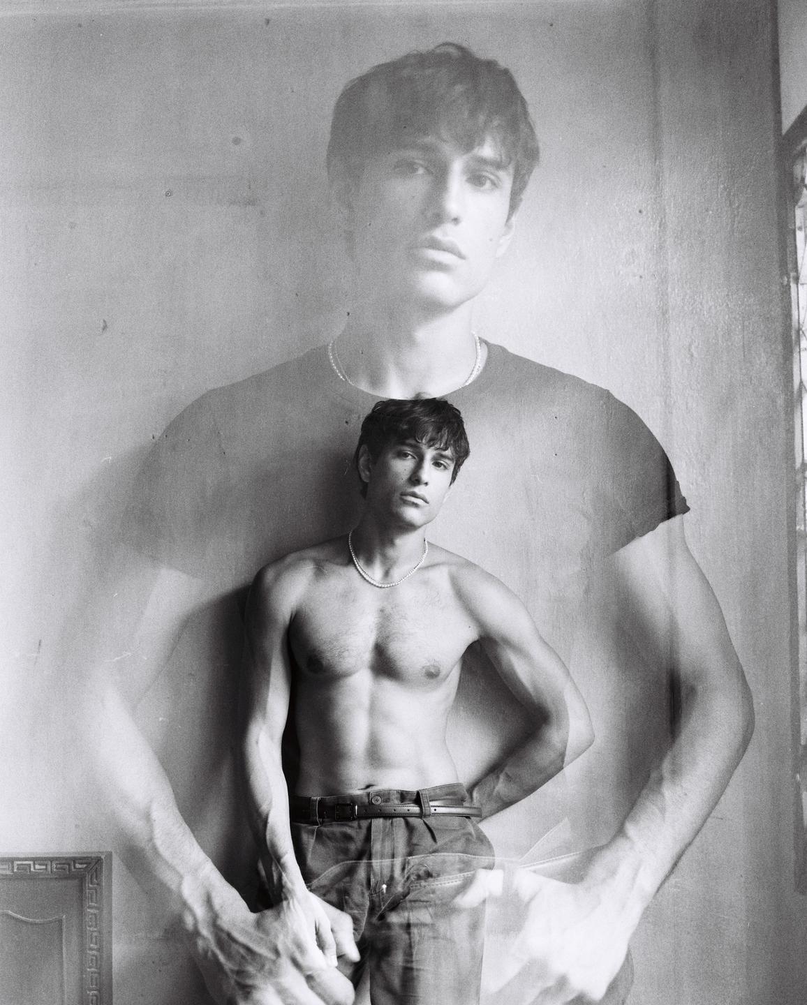 A man with a pearl necklace is captured in a double exposure, with one exposure showing him shirtless and the other showing him wearing a t-shirt.