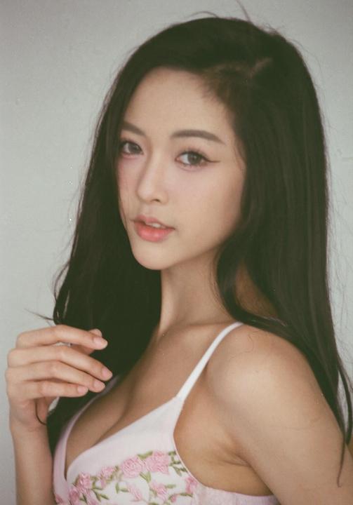A woman with long dark hair wears a light pink bra with floral embroidery.