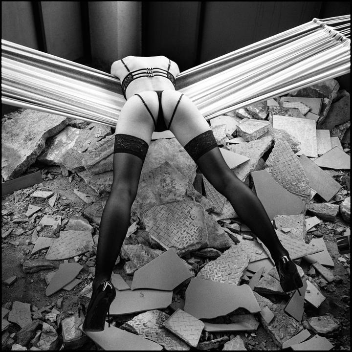 A woman in lingerie and stockings is posed over a pile of rubble.