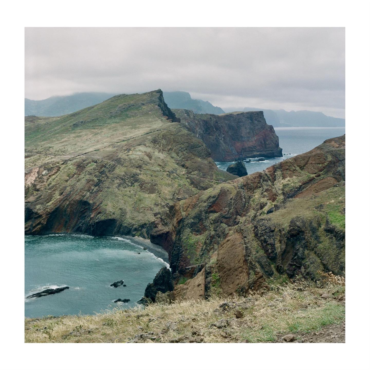 A dramatic landscape shows a rugged coastline with steep cliffs meeting the ocean under a cloudy sky.