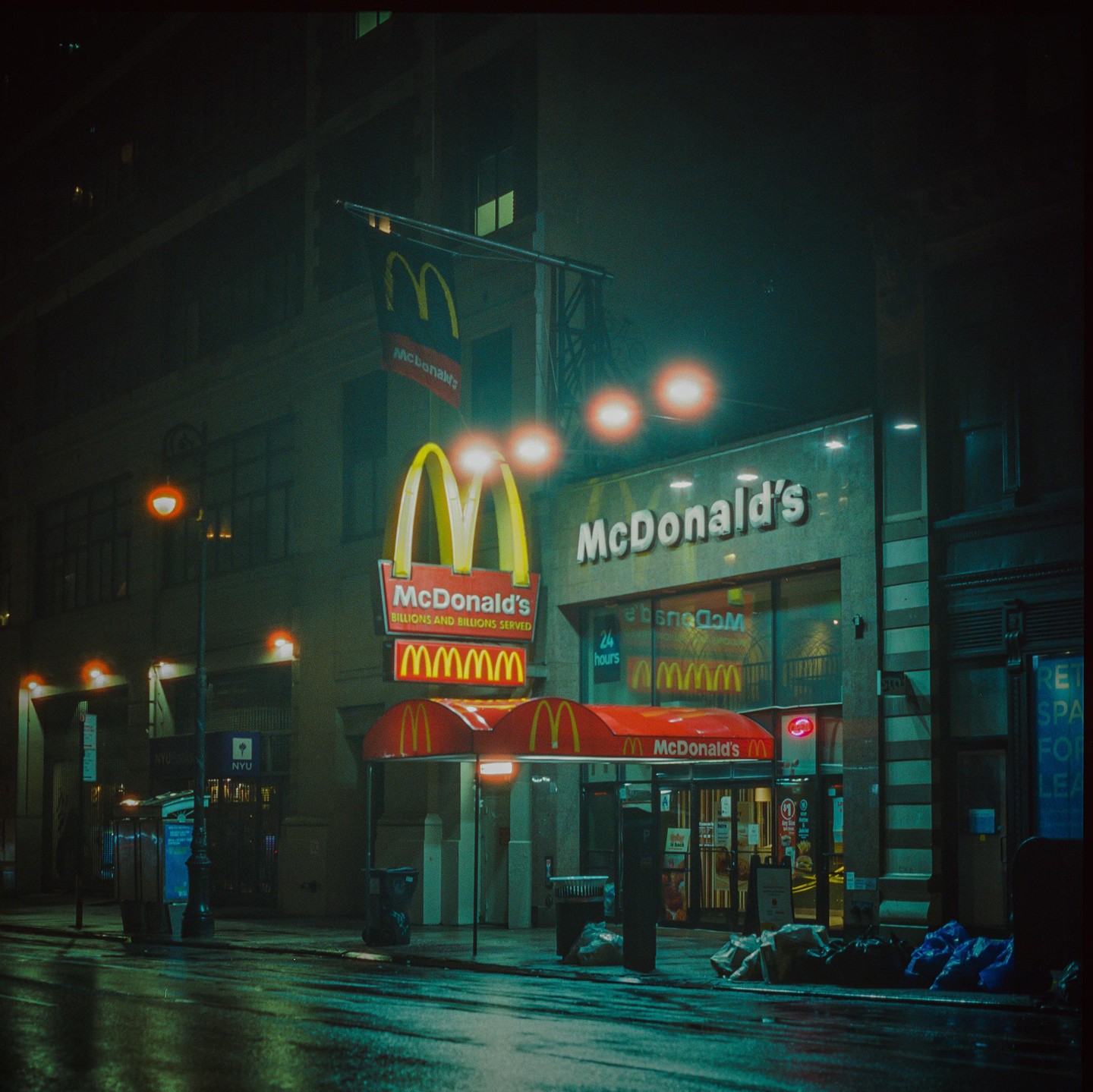 A McDonald's restaurant with its golden arches sign is illuminated at night on a wet street.