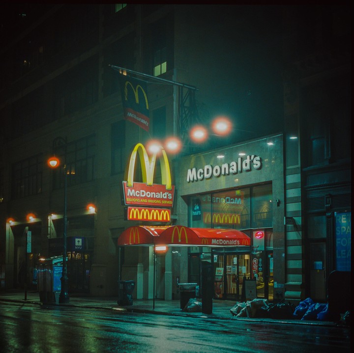 A McDonald's restaurant with its golden arches sign is illuminated at night on a wet street.