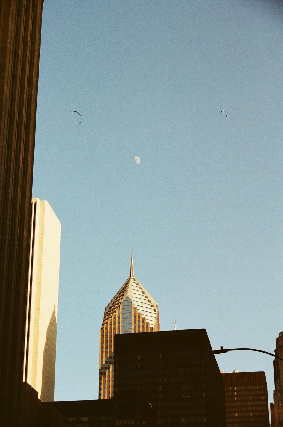 A moon is visible in the sky above several buildings in a city.