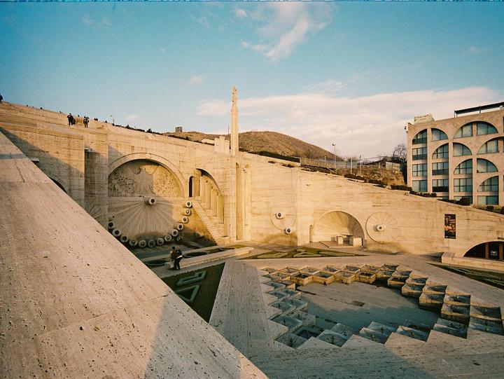 A large concrete structure with multiple levels and arches is shown under a bright sky.