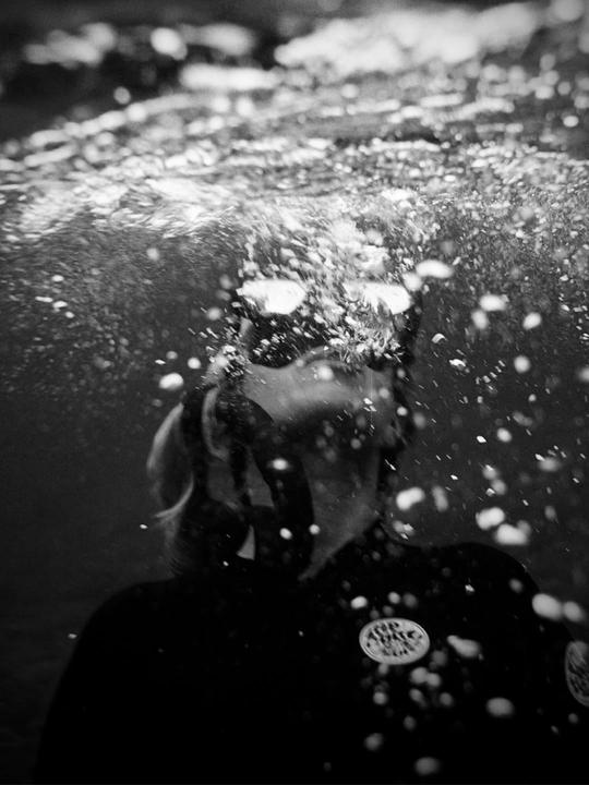 A person wearing a wetsuit and goggles is submerged in water with many bubbles around them.