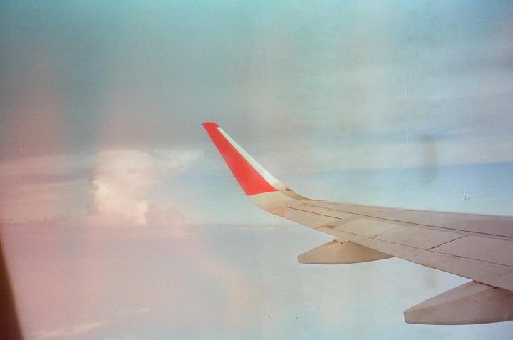An airplane wing with a red tip is visible against a cloudy sky.