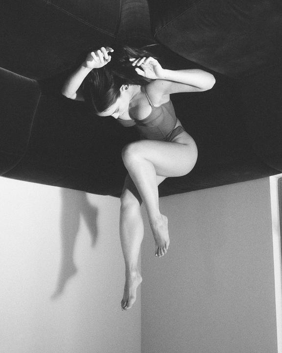 A woman in a bodysuit is suspended upside down with her legs dangling.