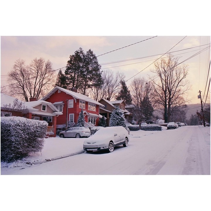 A snow-covered street with houses and cars is visible under a pale sky.