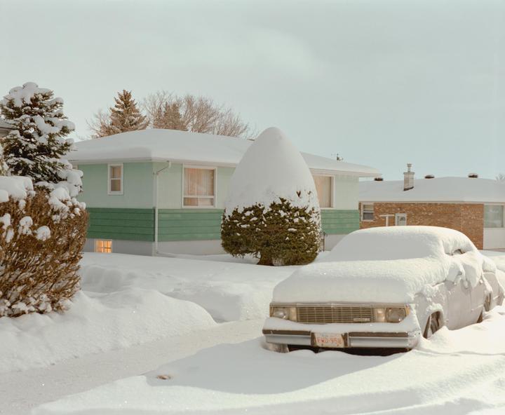 A car and a house are covered in snow on a winter day.