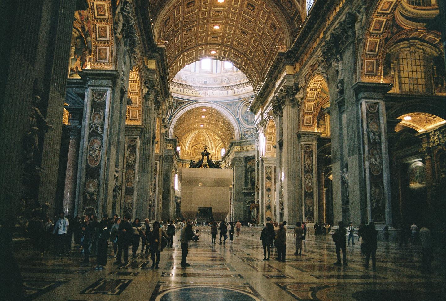 A large crowd of people stands inside a grand, ornate cathedral with a high, domed ceiling.