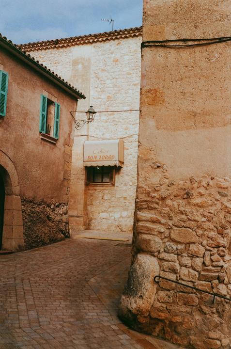 A narrow street with stone buildings and a small shop awning is visible.
