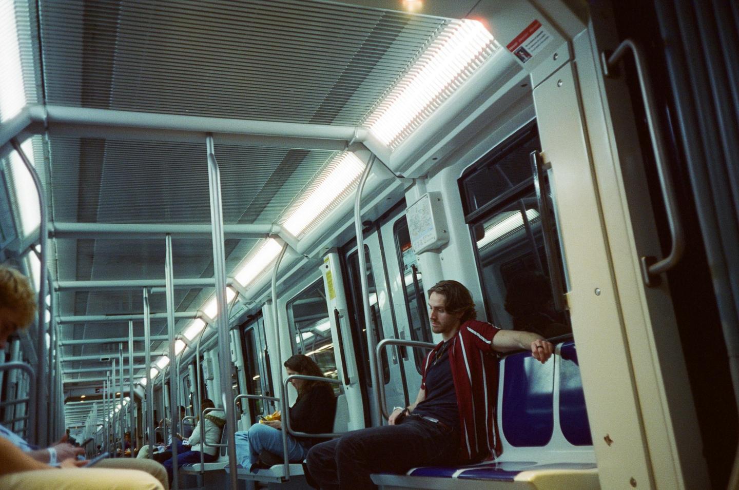 A man sits on a subway train at night, looking to his left.