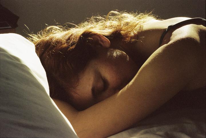 A woman with red hair is sleeping on a pillow, illuminated by warm light.