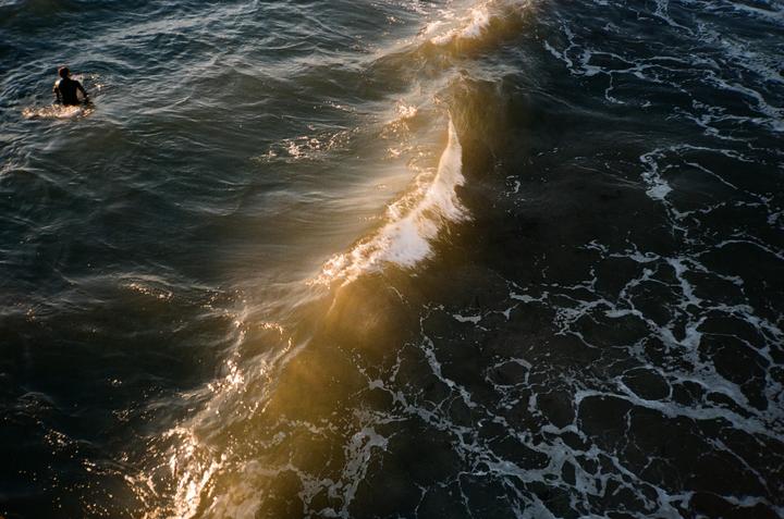 A person in a wetsuit floats in the ocean next to a breaking wave.