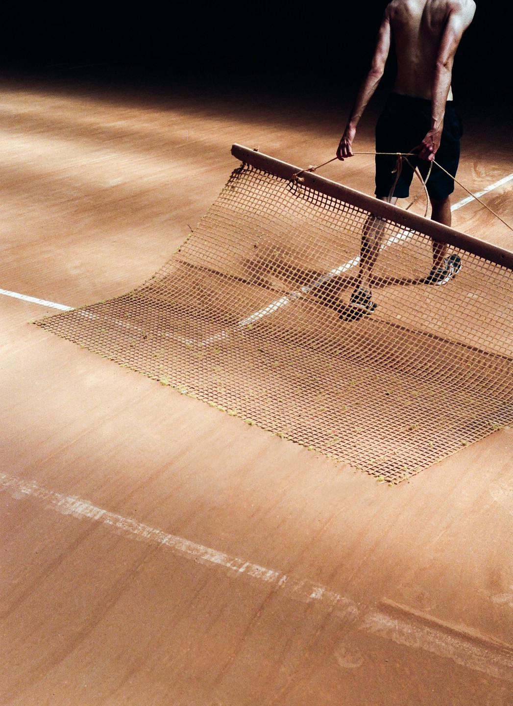 A man drags a tennis court net across a clay court.