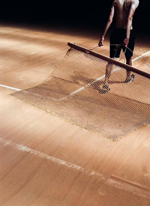 A man drags a tennis court net across a clay court.