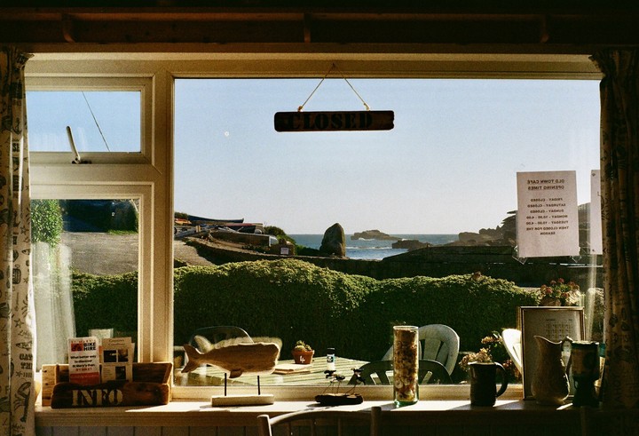 A cafe window looks out onto a sunny coastal landscape with boats and the ocean.