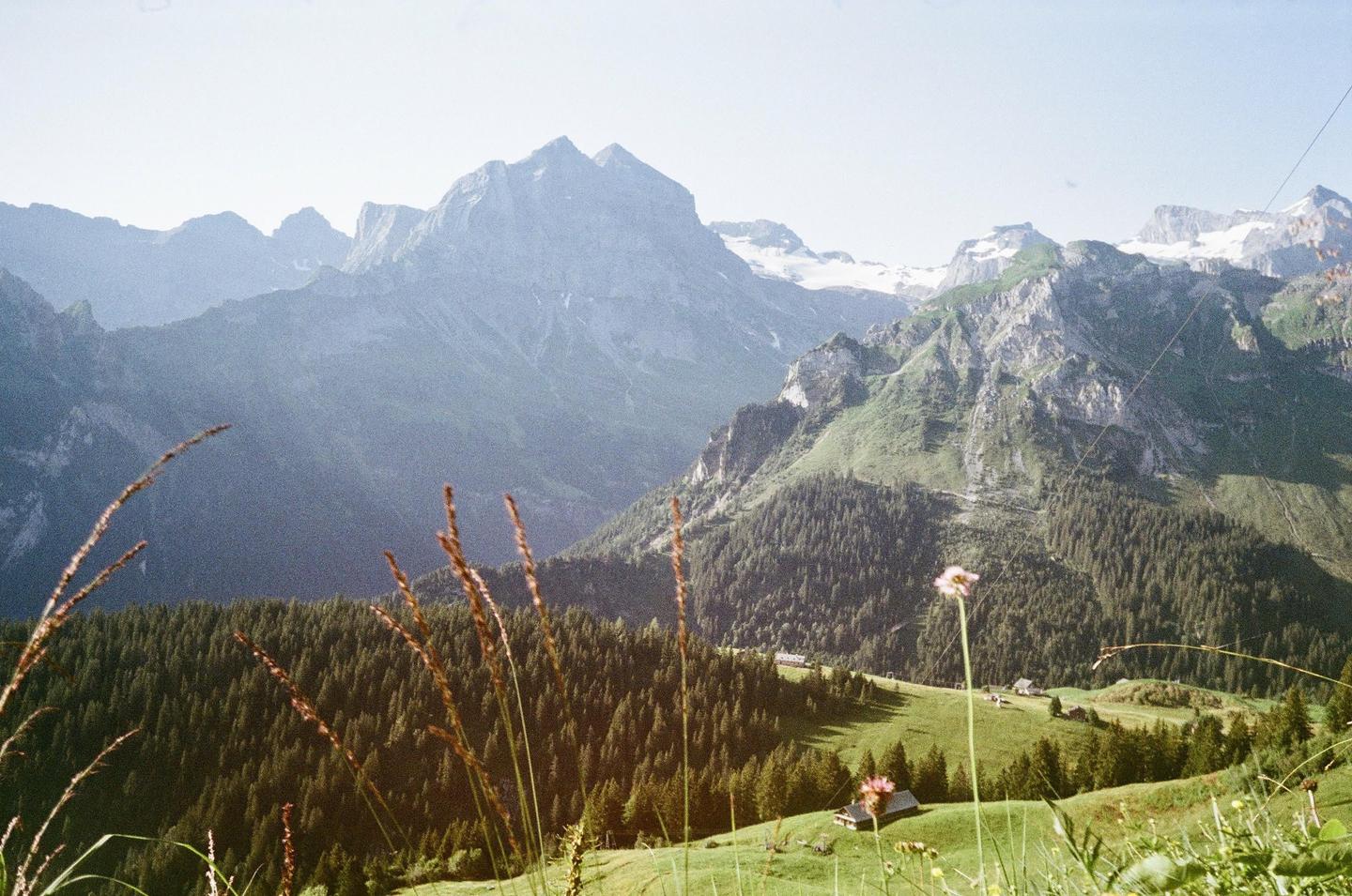 A vast mountain landscape with a valley of evergreen trees and a small village in the distance.