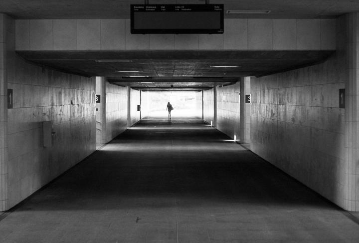 A lone figure walks towards a bright light at the end of a long, dark tunnel.