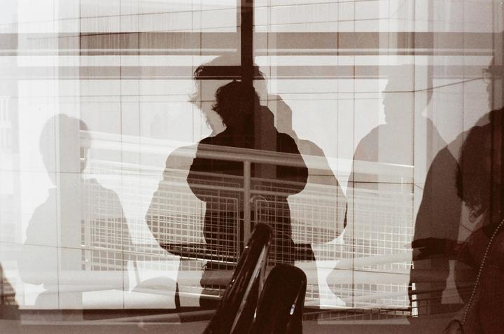Multiple exposures show a person's silhouette reflected in a window with other faint reflections.
