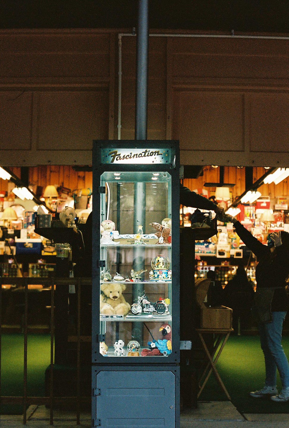 A display case filled with various trinkets and toys stands in a store with people in the background.