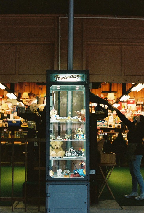 A display case filled with various trinkets and toys stands in a store with people in the background.